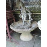 A weathered composition stone water feature in a form of a standing male figure leaning against a