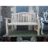 A good quality contemporary teak two seat garden bench with slatted seat and back beneath an