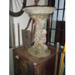 A weathered cast composition stone bird bath, the shallow circular bowl with moulded rim raised on