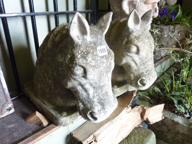 A pair of weathered cast composition stone pillar caps in the form of horses heads