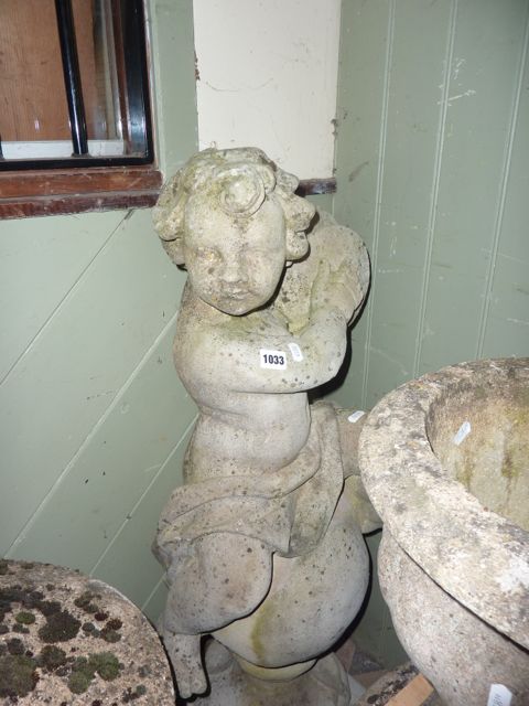 A cast composition stone garden statue in the form of a cherub astride a sphere playing cymbals