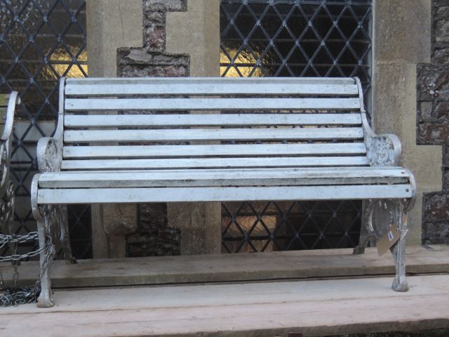 An old garden bench, the painted timber slatted seat and combined back raised on decorative