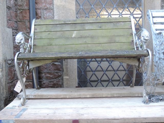 A two seat garden bench with weathered timber slatted seat and combined back raised on decorative