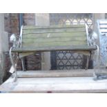 A two seat garden bench with weathered timber slatted seat and combined back raised on decorative