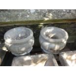 A pair of cast composition stone garden urns with circular lobed bowls and pedestal supports