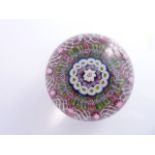A Millefiori glass paperweight with central white flower encased within alternating stars and