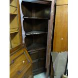 An Ercol dark elm freestanding corner cupboard the lower section enclosed by a quarter panelled door