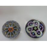 Two black ground millefiori glass paperweights, one with interlinked pink and yellow floral