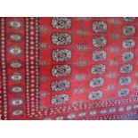 A machine woven fringed rug in the Persian style with deep red ground and multimedallion centre in