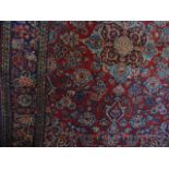 A Persian style red wool carpet with geometric detail within running borders with abstract floral