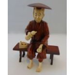 An antique figure of a seated Oriental male, principally in timber, with incised detail to