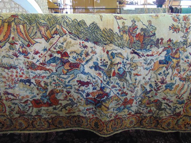 A cream ground wool rug with detail depicting a battle scene, figures on horseback accompanied by