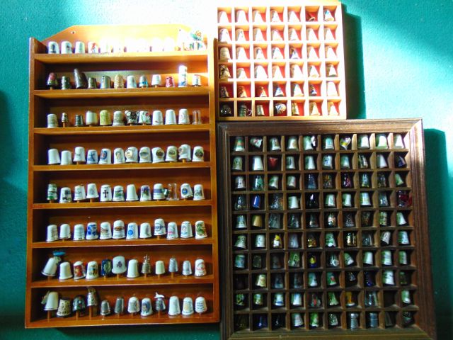 Three display racks containing an extensive collection of ceramic, glass, metal and other thimbles