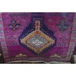 A coarse woven wool rug in the Persian manner with a plum coloured ground decorated in geometric