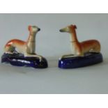 Two 19th century Staffordshire Pottery inkwells in the form of recumbent greyhounds raised on blue