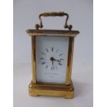 A miniature brass cased carriage clock with bevelled glazed panelled sides enclosing a white