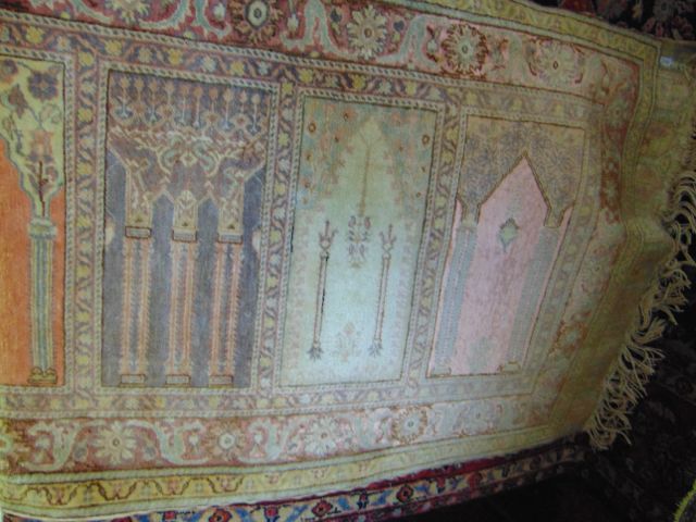 A fringed wool work runner with central panels detailing architectural decoration in shades of pink,