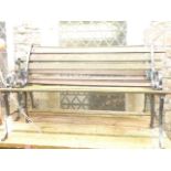 A two seat garden bench with weathered timber slatted seat and back raised on decorative cast and