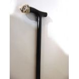 An ebonised walking stick with the shaped handle terminating in an applied brass coloured cap in the