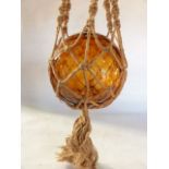 A large amber glass buoy converted to a lamp contained within woven hessian netting