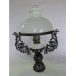 An oil lamp with opaque glass fount set within an elaborate pierced ironwork stand and frame with