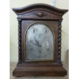 An Edwardian oak bracket clock with barley twist supports, the arched silvered dial with regulator