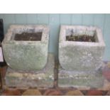 A pair of weathered carved granite garden planters of square cut and tapered form raised on square