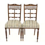 A pair of late Victorian walnut and inlaid dining chairs each with an inlaid top rail above a