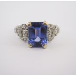 A TANZANITE AND DIAMOND RING claw set to the centre with an emerald-cut tanzanite weighing