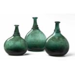 THREE PERSIAN GREEN-GLASS SADDLE FLASKS in sizes, each of typical form, the largest 26,5cm high (3)