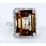 A TOPAZ AND DIAMOND RING centred with an orange-brown emerald-cut topaz weighing approximately 14.