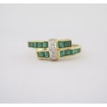 AN EMERALD AND DIAMOND RING of cross-over design, channel set to the centre with carré-cut