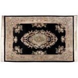 A CHINESE CARPET, MODERN the black field with a bold floral medallion depicted in ivory, rose,