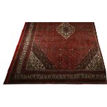 A HAMADAN CARPET, PERSIA, CIRCA 1960 the red field with a stepped floral medallion depicted in ivory