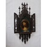 Carved wooden frame with 2 doors opening to reveal an oval china plaque of Christ.