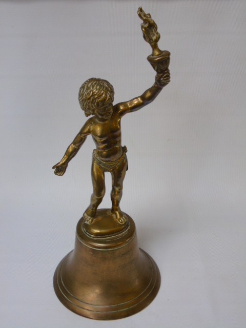 A bronzed bell with brass handle in the form of a boy holding a torch