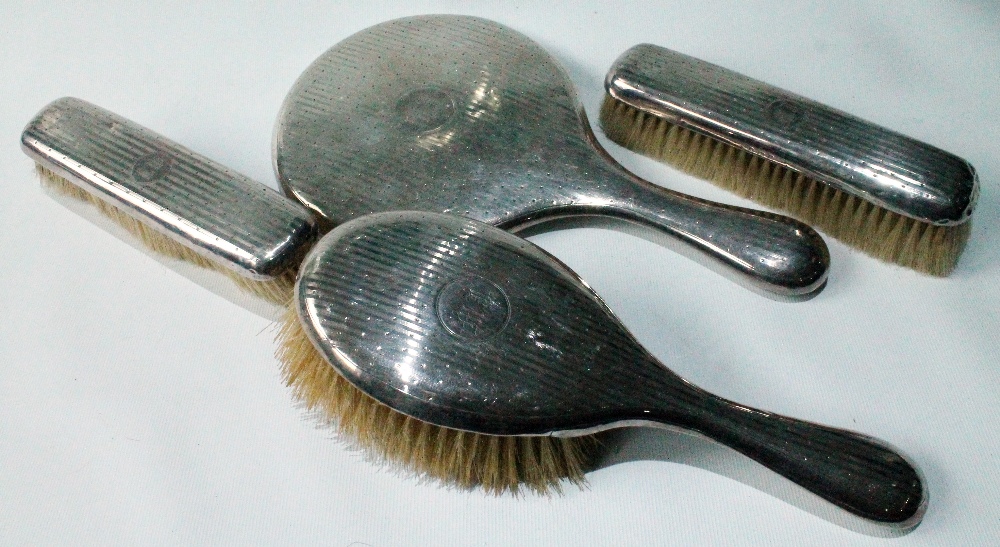Three Edwardian silver-mounted brushes and a hand mirror, engine-turned, Birmingham 1907.