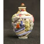 Chinese famille rose snuff bottle with relief decoration of figures in a palace garden setting.