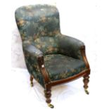 Victorian carved mahogany armchair with green floral upholstery on turned legs and brass castors
