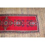 An Iranian wool runner, worked with a central foliate design against a red ground,