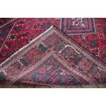 A Caucasian wool carpet, worked with a foliate panel design against a red ground,