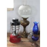 A brass oil lamp with frosted shade; a tilly lamp with red enamel base,