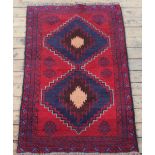 A Baluch wool rug, worked with two panels against a red ground,