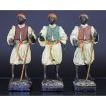 Three late 19th Century cold painted spelter figures of Nubian man servants, in traditional attire,