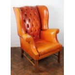 A George III style mahogany wing back arm chair, with tan leathrette button back upholstery,
