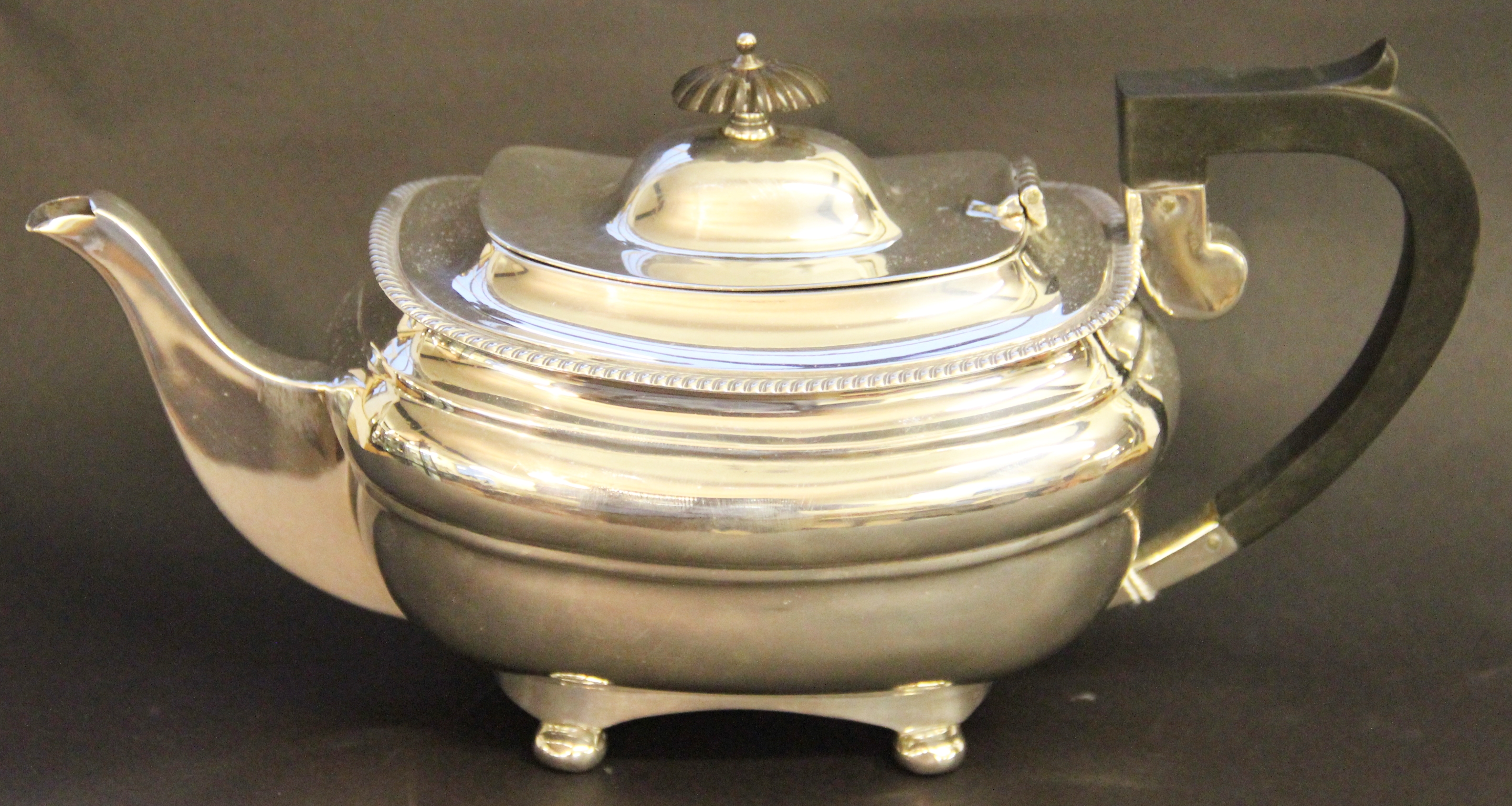 A George V silver tea pot, Sheffield, 1912, with ebonised finial and handle, on ball toes, 26.