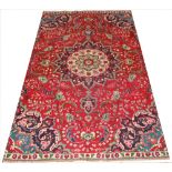 A Persian Tabriz wool rug, worked with an a central medallion against a red ground,