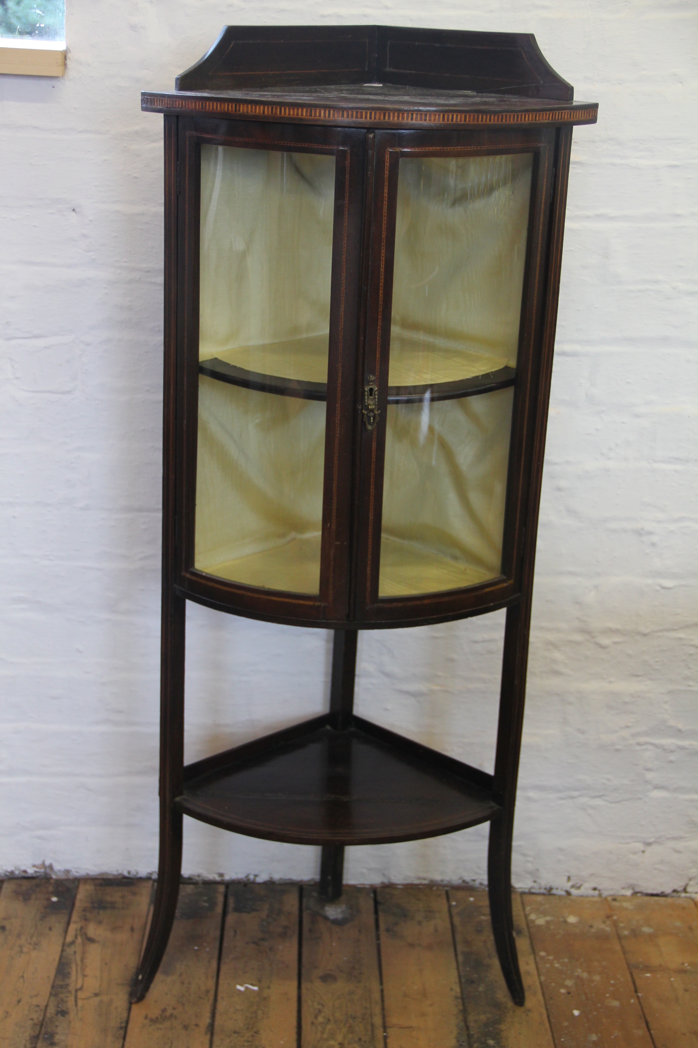 An Edwardian inlaid mahogany bow front corner cabinet, with undertier, on out-swept legs,