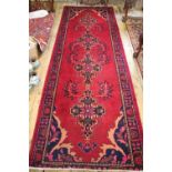 A Persian wool runner worked with a foliate design against a red ground,