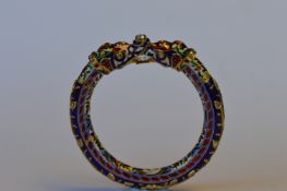 A heavy Eastern enamelled bangle decorated with flowers and leaves in the form of two serpents